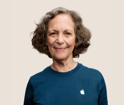 Retrato de uma funcionária sorridente da Apple Retail, com cabelos grisalhos e ondulados.