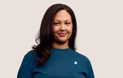 Retrato de uma funcionária sorridente da Apple Retail, com cabelos longos e escuros.