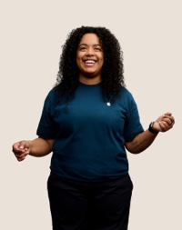 Retrato de uma funcionária sorridente da Apple Retail, com cabelos longos, escuros e cacheados.