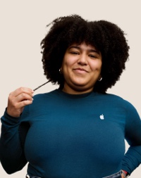 Retrato de uma funcionária sorridente da Apple Retail, com cabelos longos, escuros e cacheados.