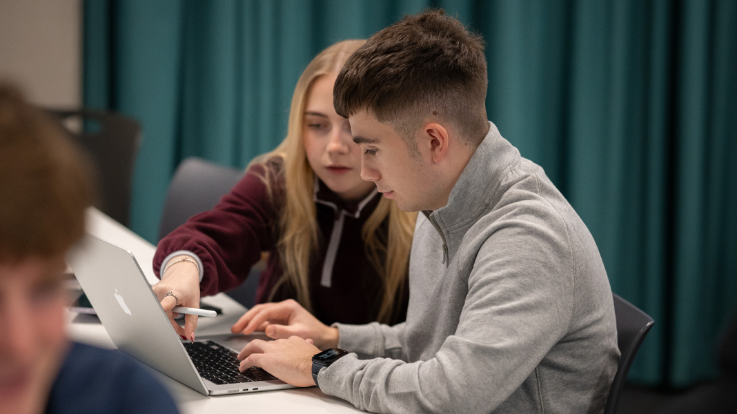 Studenter samarbeider på en MacBook, og en peker på skjermen mens en annen skriver